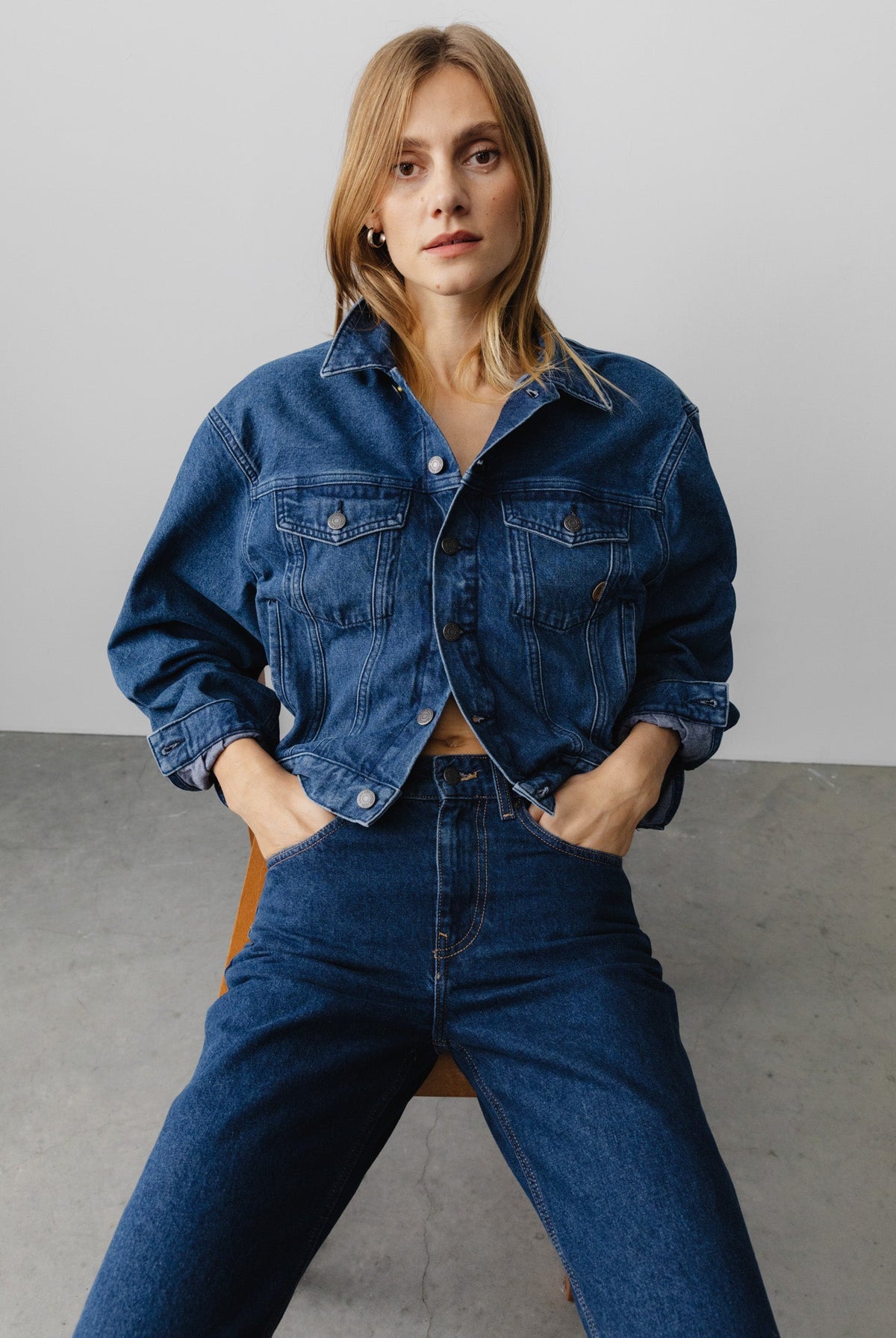 Woman wearing a classic denim jacket with matching high-waisted jeans, styled in a casual fashion on a minimalist background.