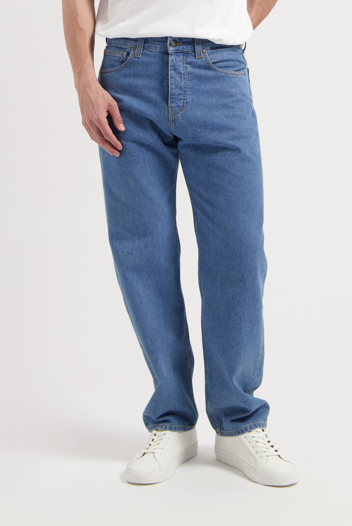 Sustainable MUD Jeans in classic blue denim, featuring an ethical design, paired with black shoes and a charcoal sweater.