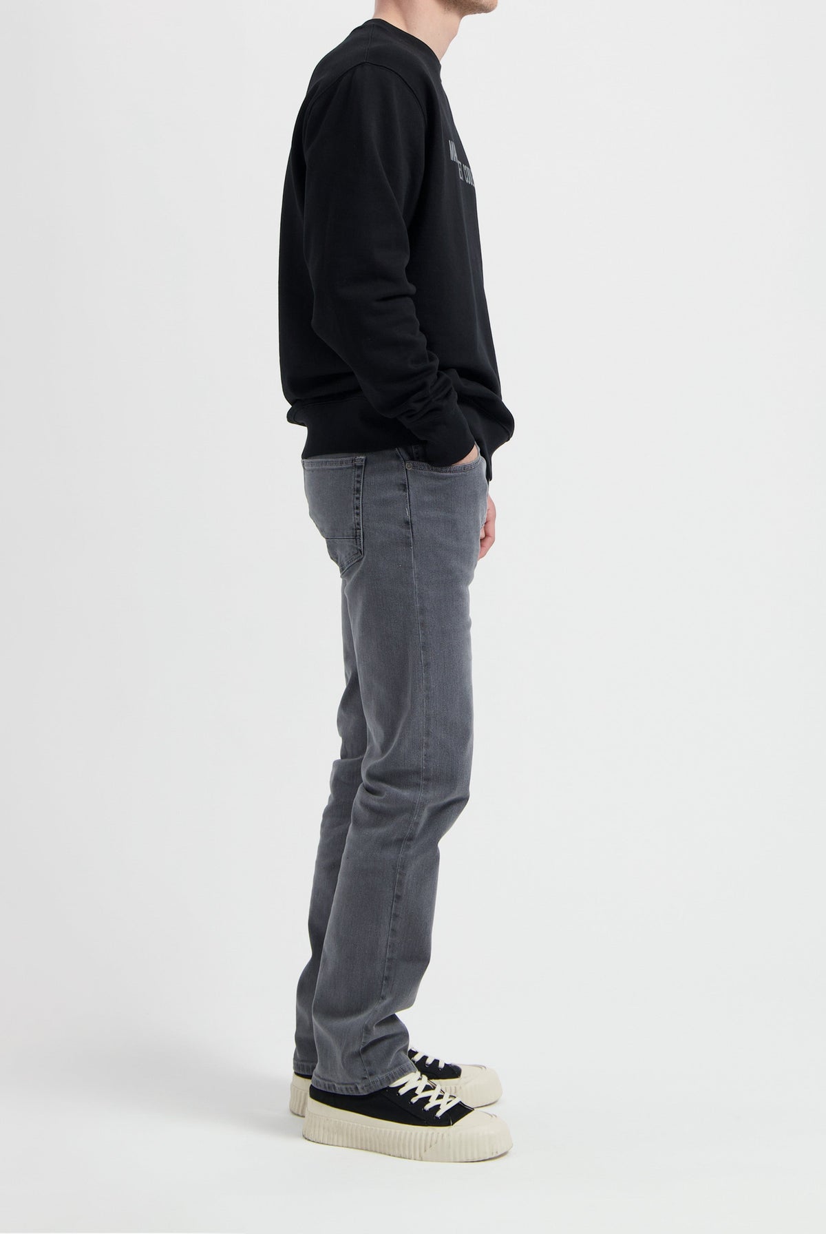 Sustainable MUD Jeans in gray denim, crafted ethically from organic cotton, paired with a black sweatshirt and sneakers.
