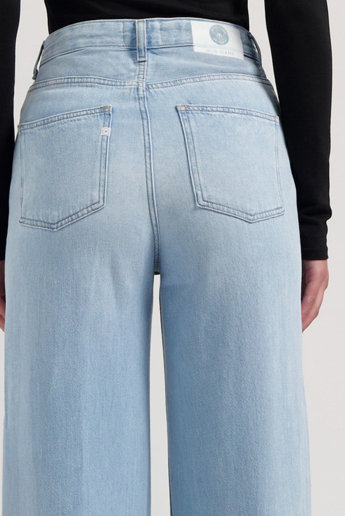 Rear view of light blue, high-waisted MUD Jeans in sustainable denim, showcasing a wide-leg fit paired with a sleek black top.