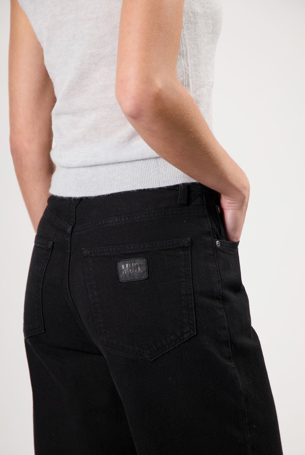 Model wearing black MUD Jeans made from organic cotton, featuring a light gray sleeveless top for an eco-friendly fashion look.