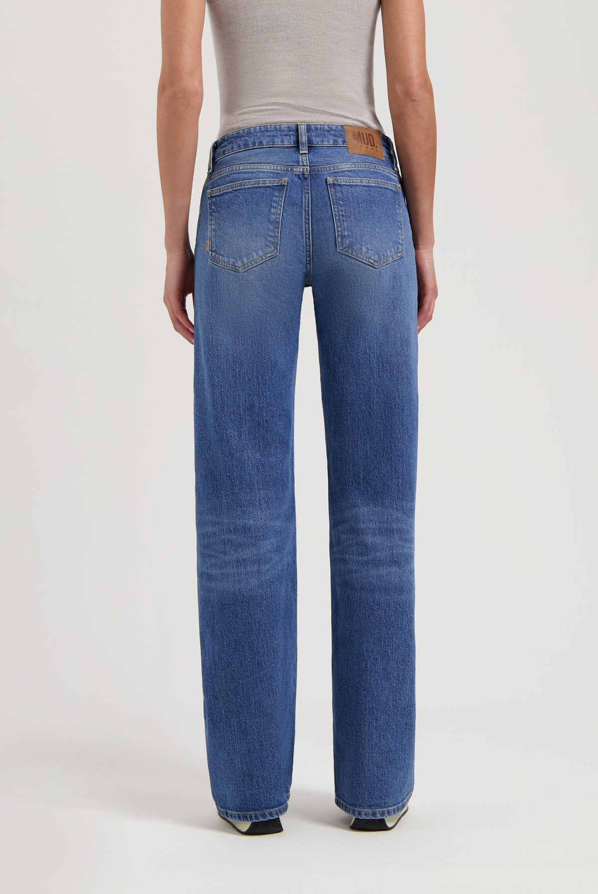 Back view of eco-friendly blue denim jeans by MUD Jeans, featuring a straight-leg fit paired with a beige sleeveless top.