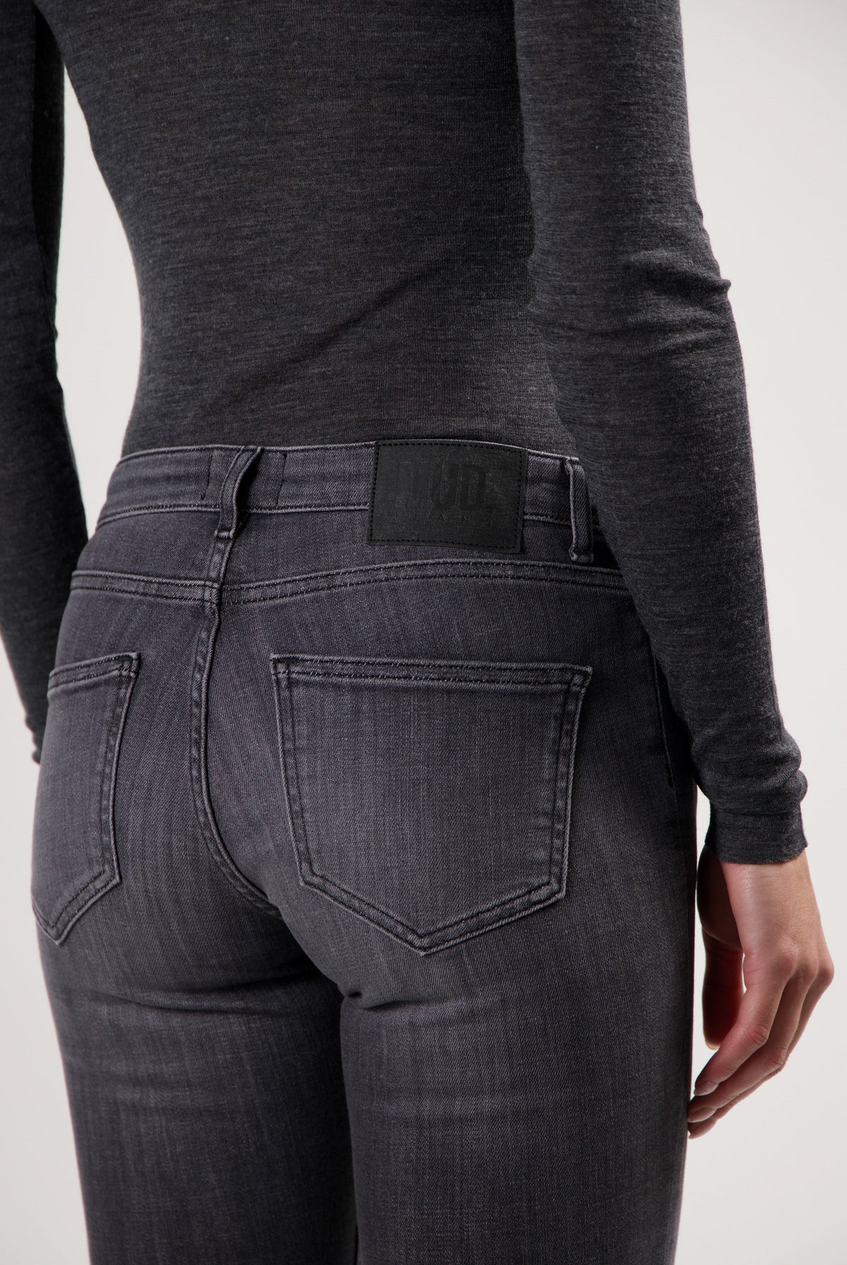 Dark gray MUD Jeans made from organic cotton, displaying a pair of slim-fit denim jeans worn with a long-sleeve gray top.