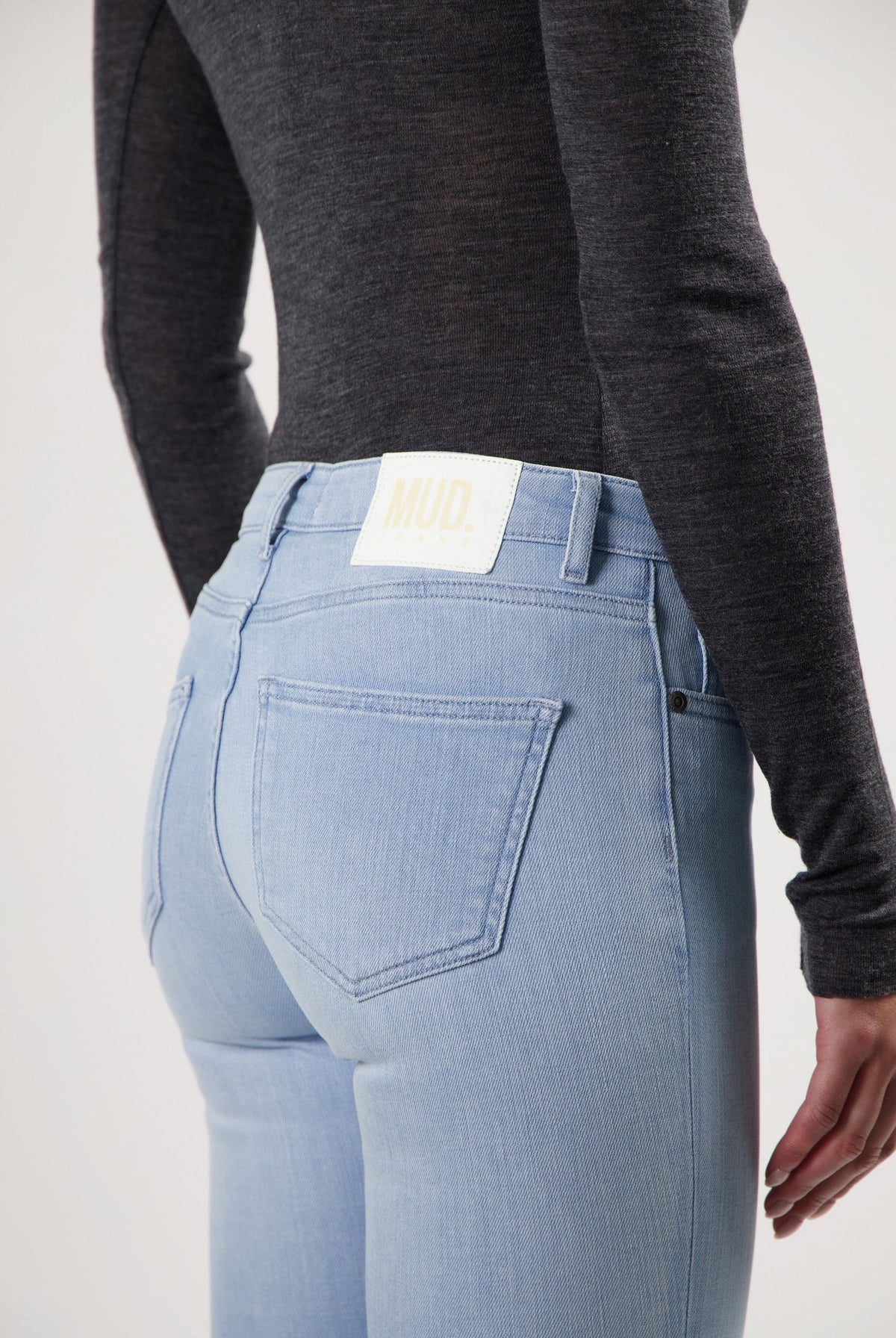 Light blue, eco-friendly MUD Jeans made from organic cotton, featuring a back view with a black long-sleeve top.