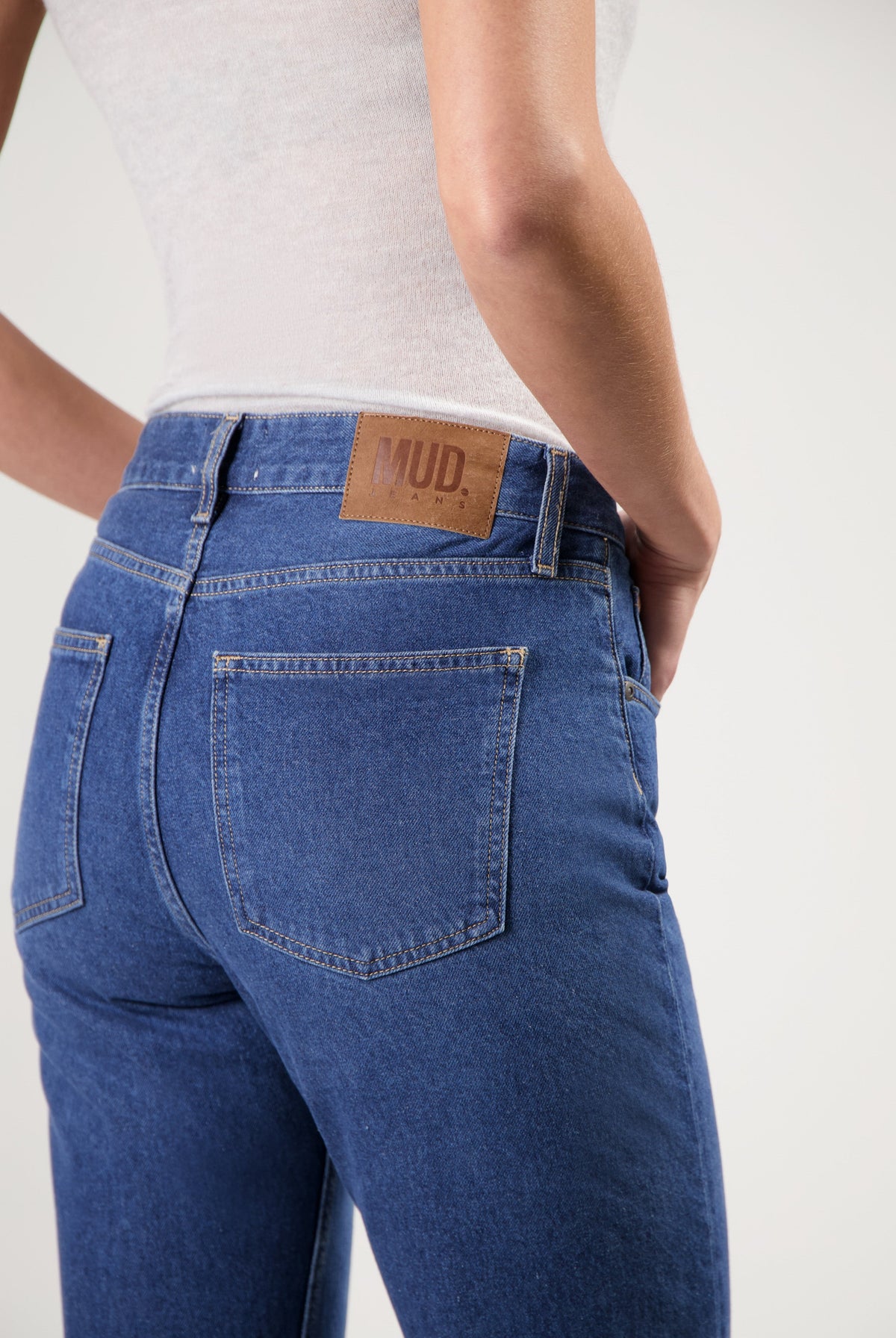 Dark blue MUD Jeans crafted from organic cotton, featuring back pocket stitching, worn with a white sleeveless top.
