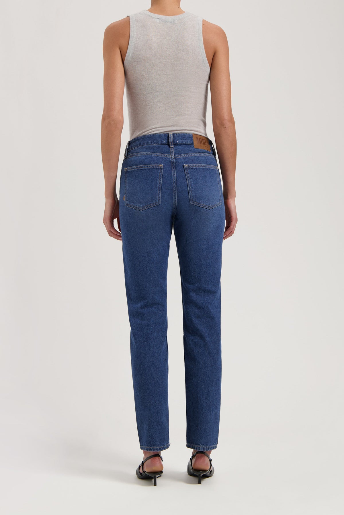 Person wearing sustainable dark blue denim jeans with a white sleeveless top, showcasing the back view and fit.