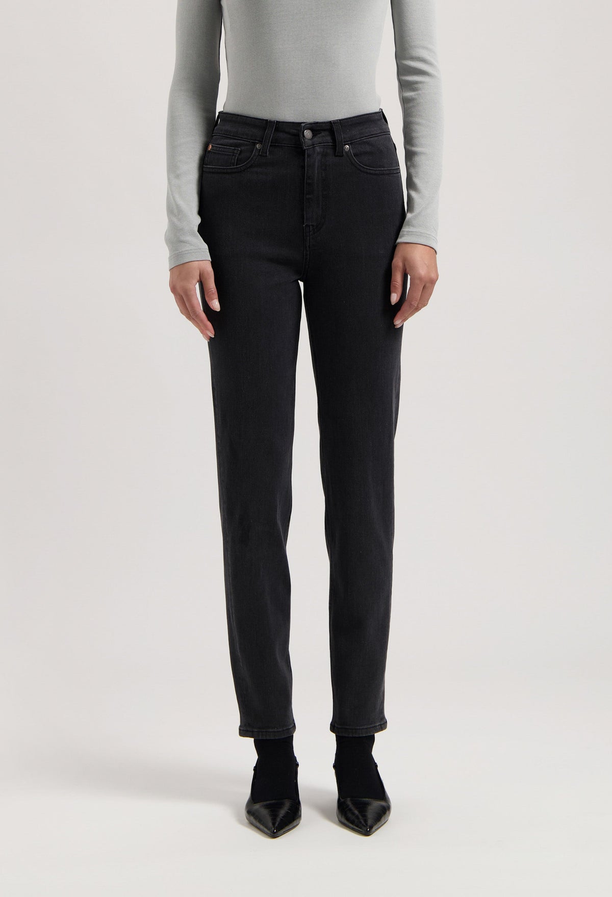 Person wearing black straight-leg jeans with a high-waist fit, paired with a light gray long-sleeve shirt and black heels.