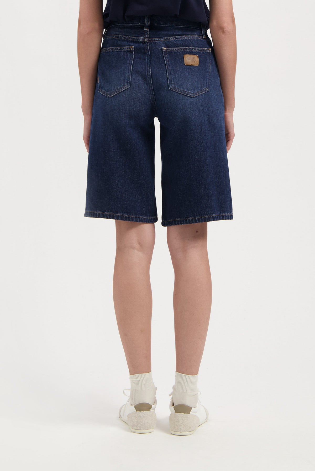 Back view of dark blue MUD Jeans denim shorts, showcasing high-waisted design with two pockets, paired with a navy top.