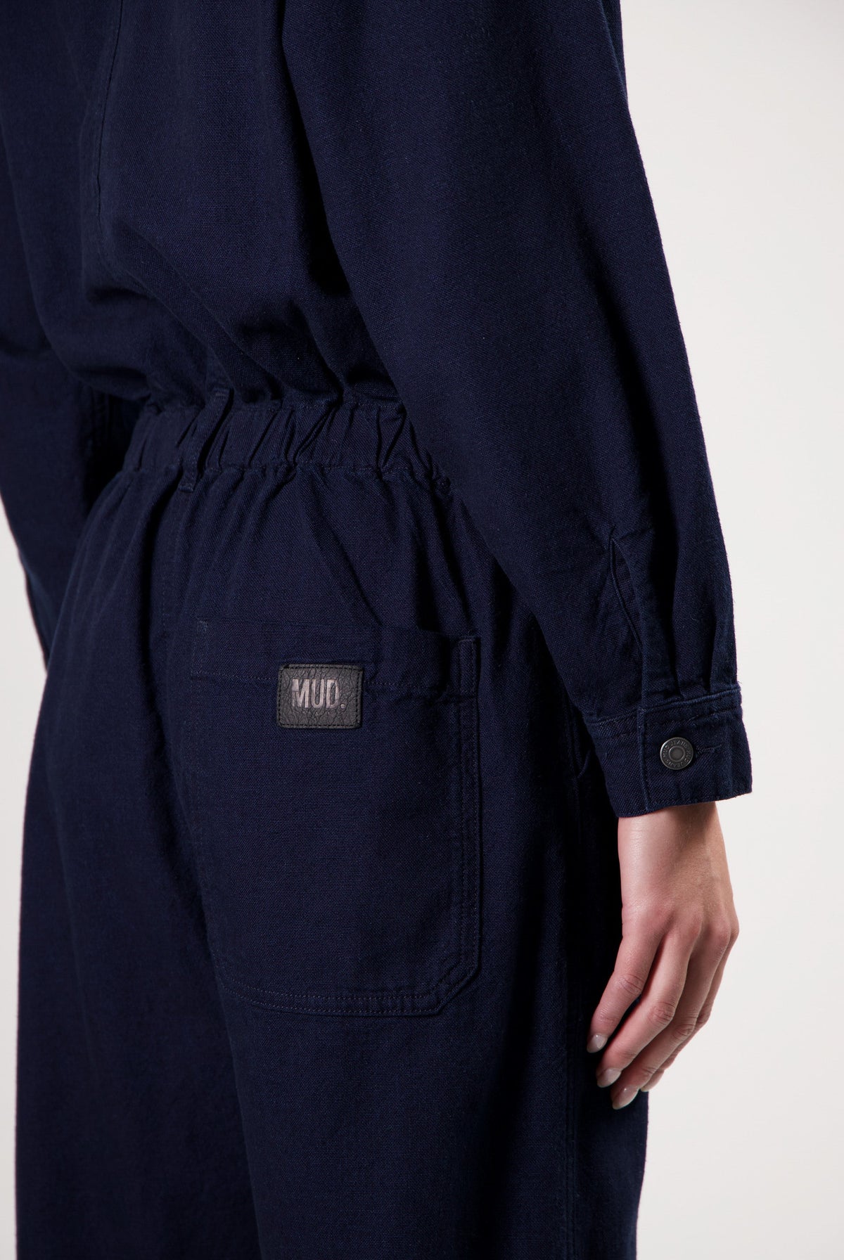 Navy blue MUD denim jumpsuit with elastic waistband and pocket detailing, long sleeves with button cuffs.