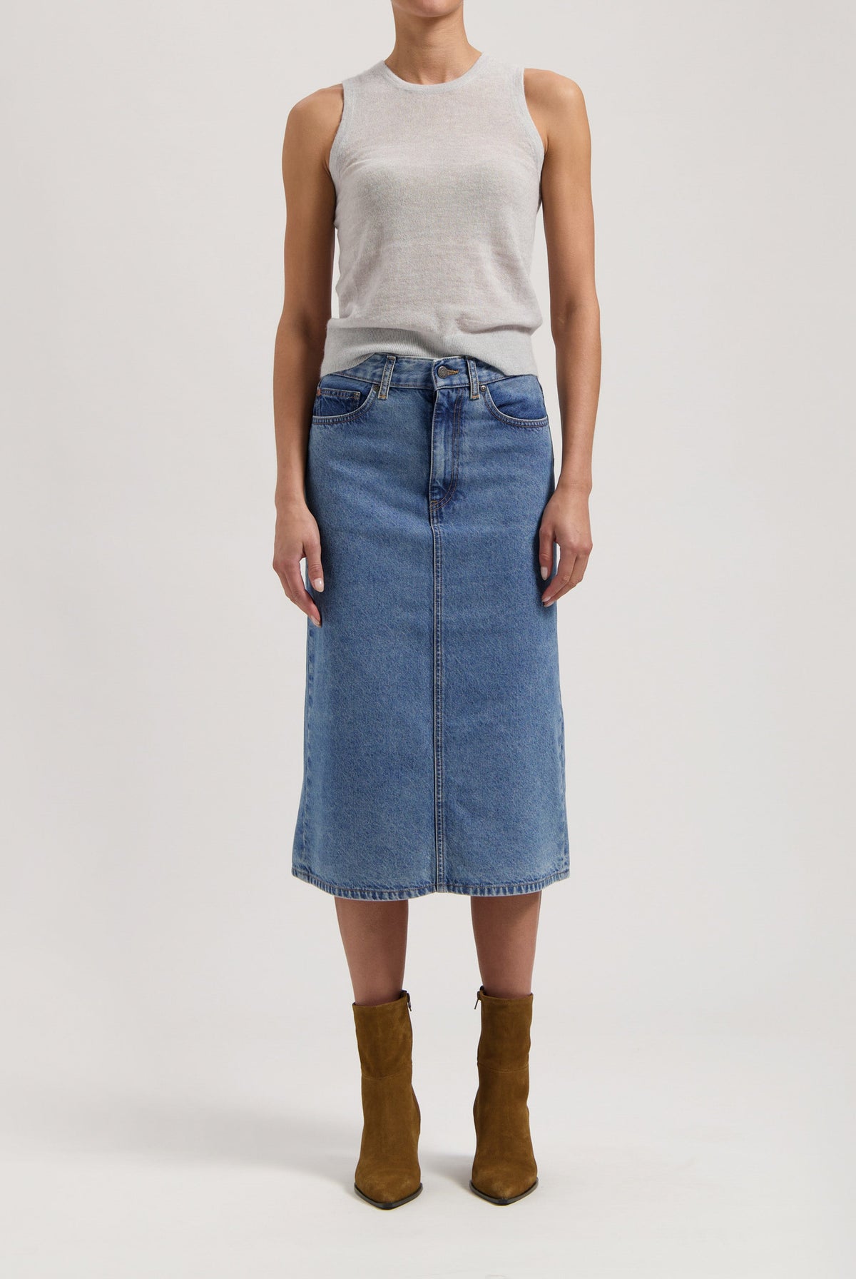 Mid-length denim skirt in blue paired with a sleeveless gray top, styled with brown suede ankle boots on a white background.