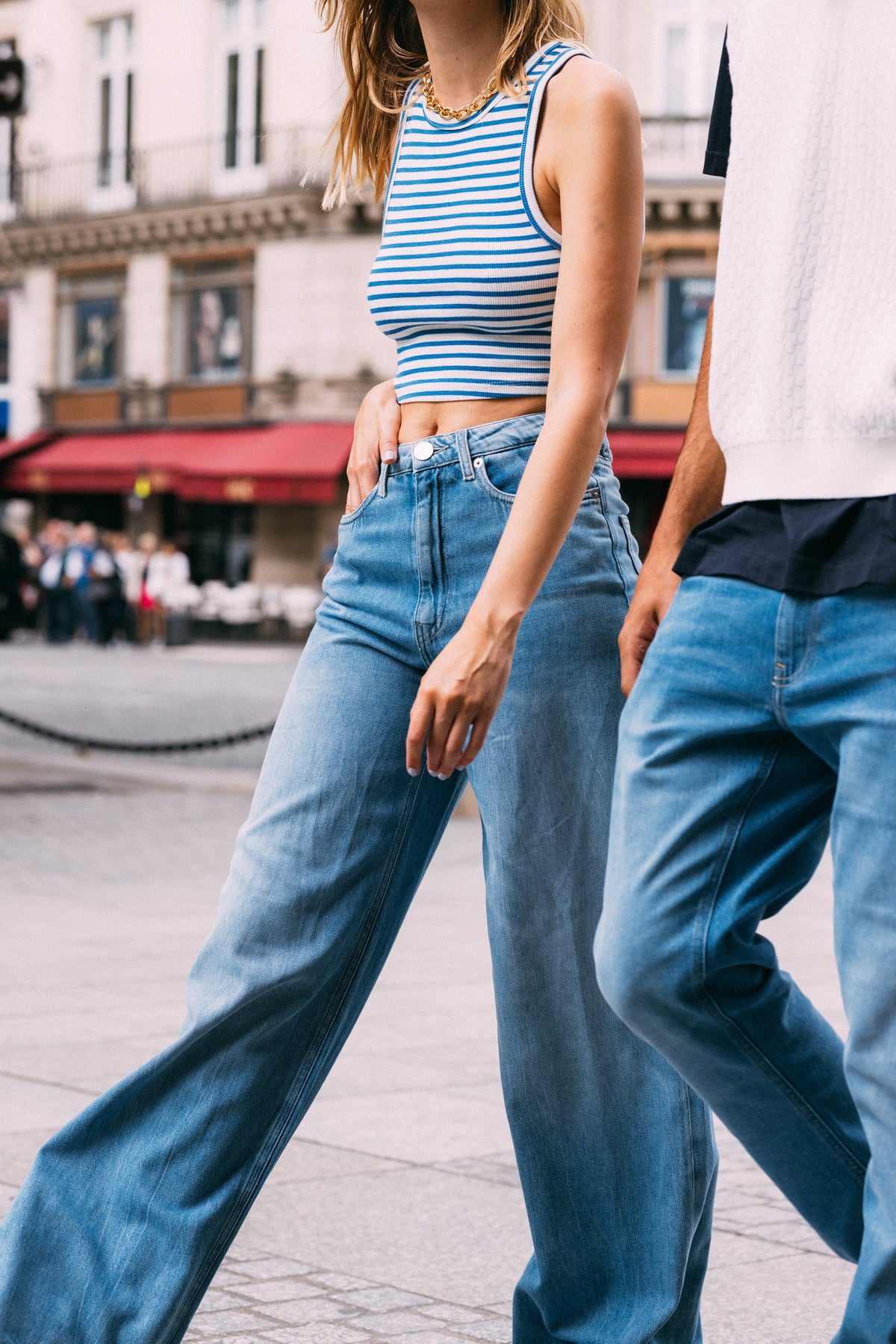Casual streetwear featuring light blue high-waisted jeans paired with a blue and white striped sleeveless crop top.