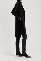 Black oversized shirt dress paired with dark gray, straight-leg jeans and pointed black kitten heels.