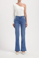 One-shoulder white top with long sleeve paired with high-waisted blue flare jeans, styled with white pointed heels.