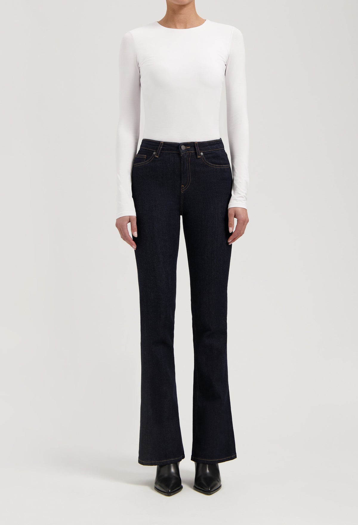 Woman wearing dark blue bootcut jeans with a white long-sleeve fitted top, showcasing casual chic style.