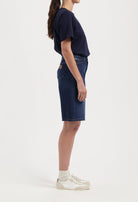 Side view of a woman wearing a stylish dark blue denim skirt paired with a navy t-shirt and white sneakers.