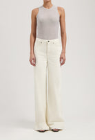 Woman wearing light gray sleeveless top paired with high-waisted, wide-leg white denim jeans, showcasing modern casual fashion.