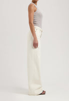 A model wearing high-waisted, wide-leg white denim jeans paired with a fitted gray tank top, showcasing a sleek side profile.