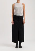 Model wearing a sleeveless gray top with a long black denim skirt, featuring a central slit, and black ankle boots.