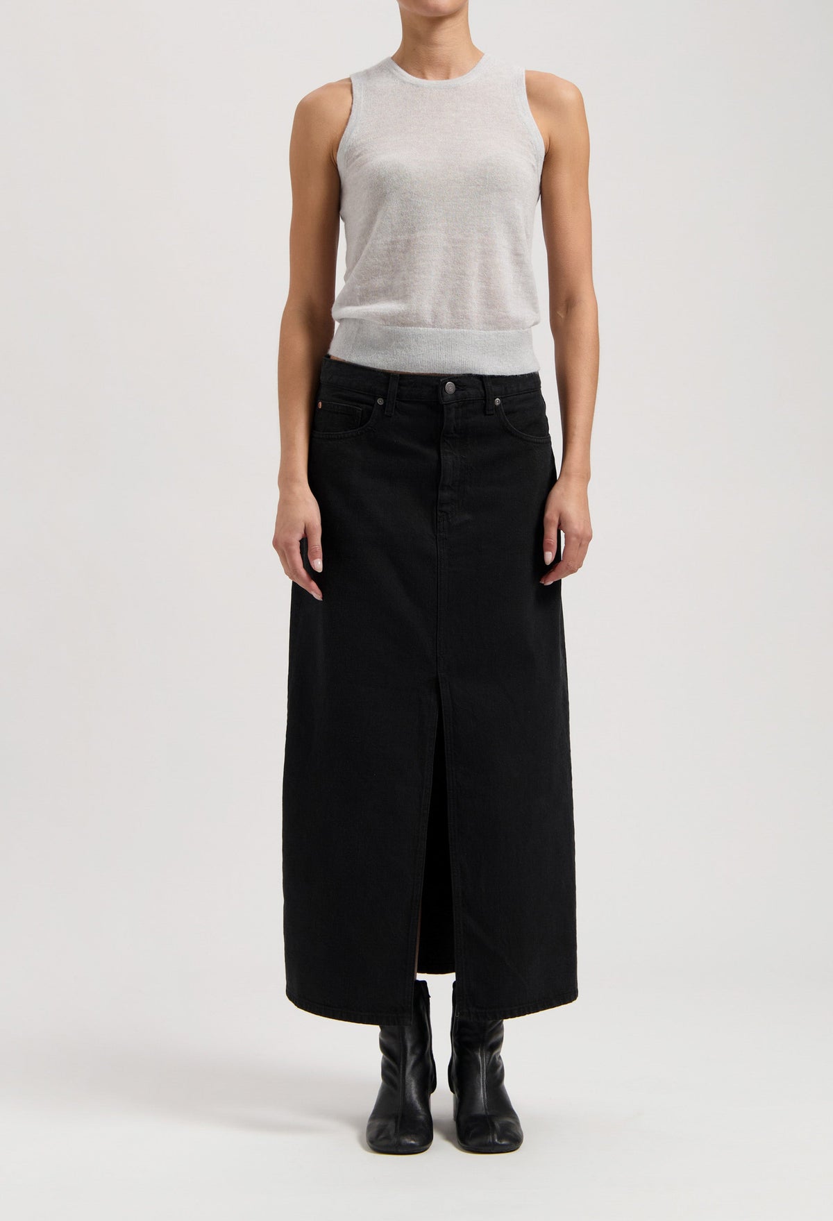Model wearing a sleeveless gray top with a long black denim skirt, featuring a central slit, and black ankle boots.