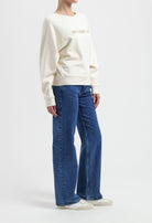 Woman modeling a cream sweatshirt with blue wide-leg jeans and white sneakers, showcasing casual and comfortable fashion.